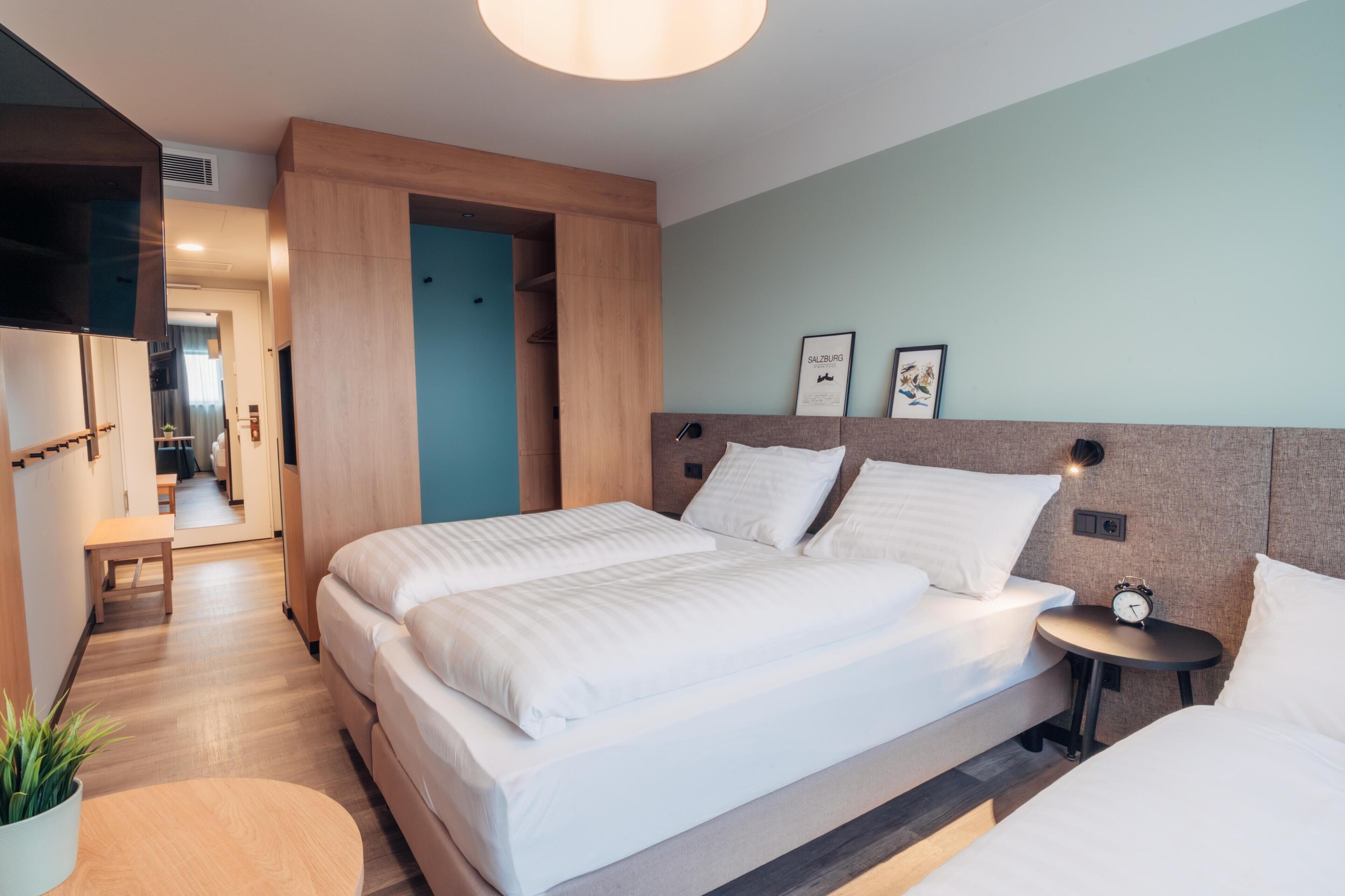 Une chambre d’hôtel moderne avec un grand lit, des tables de chevet, une télévision et une petite table agrémentée d’une plante.
