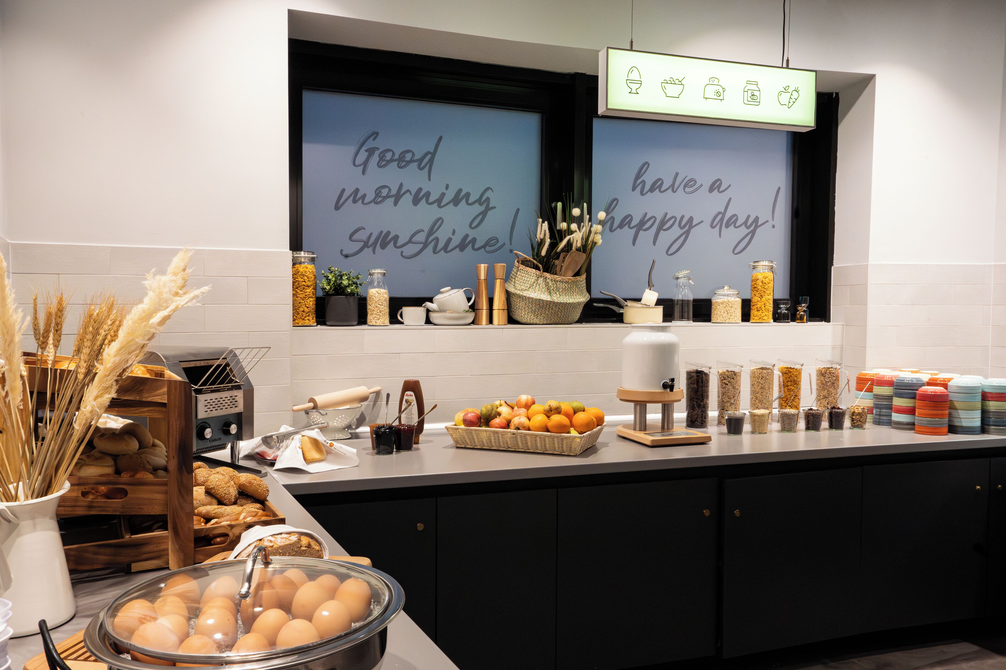 A breakfast buffet with a variety of food items, including eggs, fruits, and cereals, displayed on a counter with a sign above that reads "Good morning sunshine! Have a happy day!"