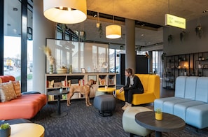 A modern hotel lobby with seating areas, a dog, and a 'Harry's Hotel' sign.