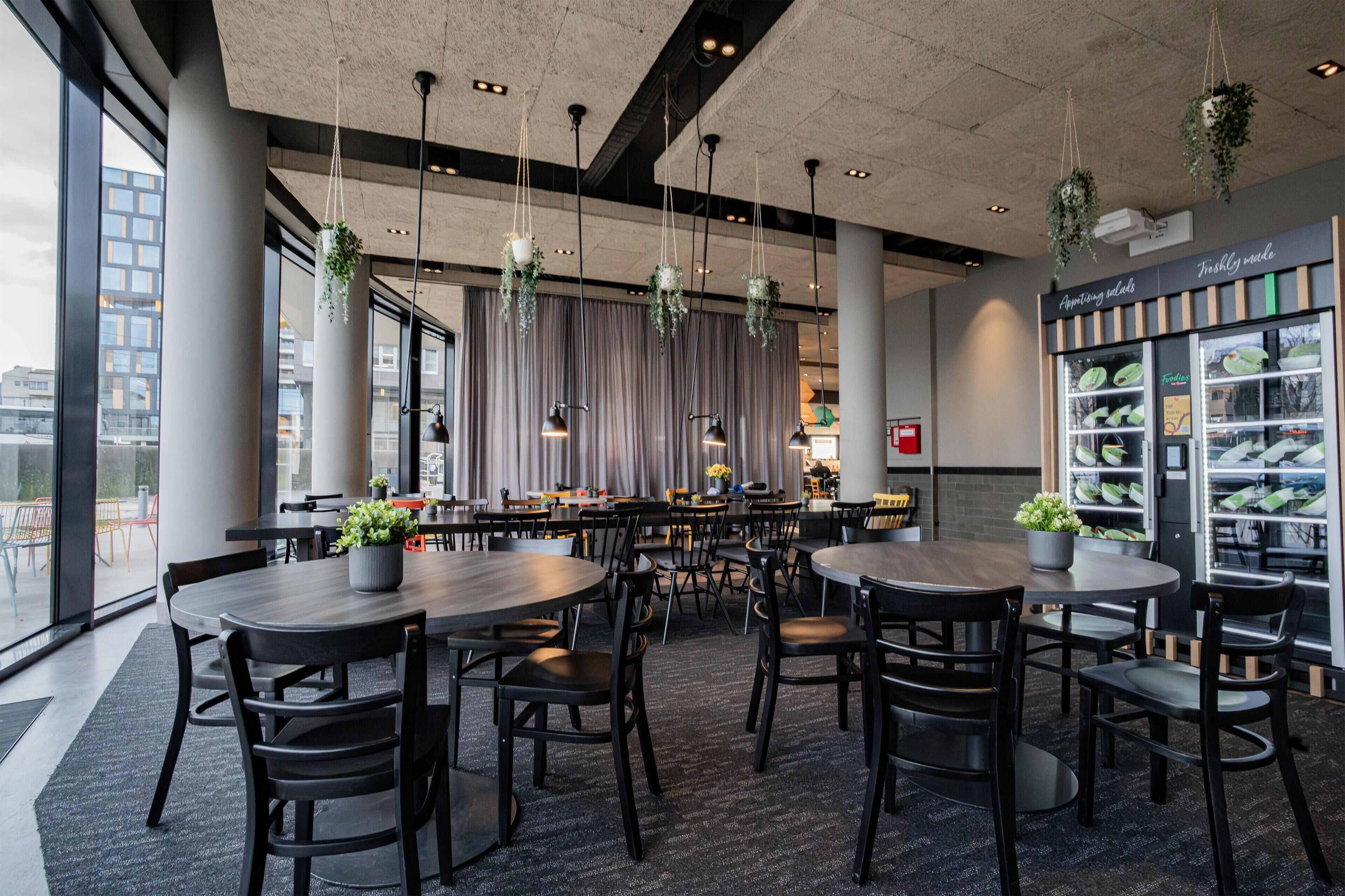 A modern restaurant with round tables and chairs, hanging plants, and a view of the city.