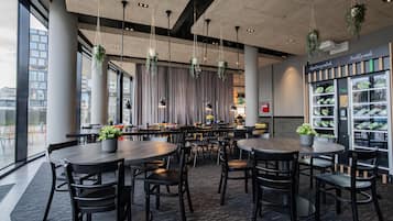 A modern restaurant with round tables and chairs, hanging plants, and a view of the city.