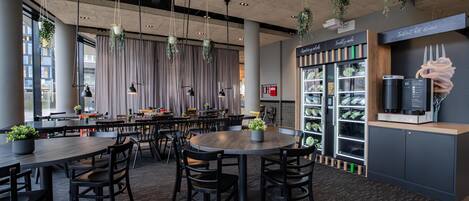 A modern dining area with round tables and chairs, hanging plants, and a coffee station.