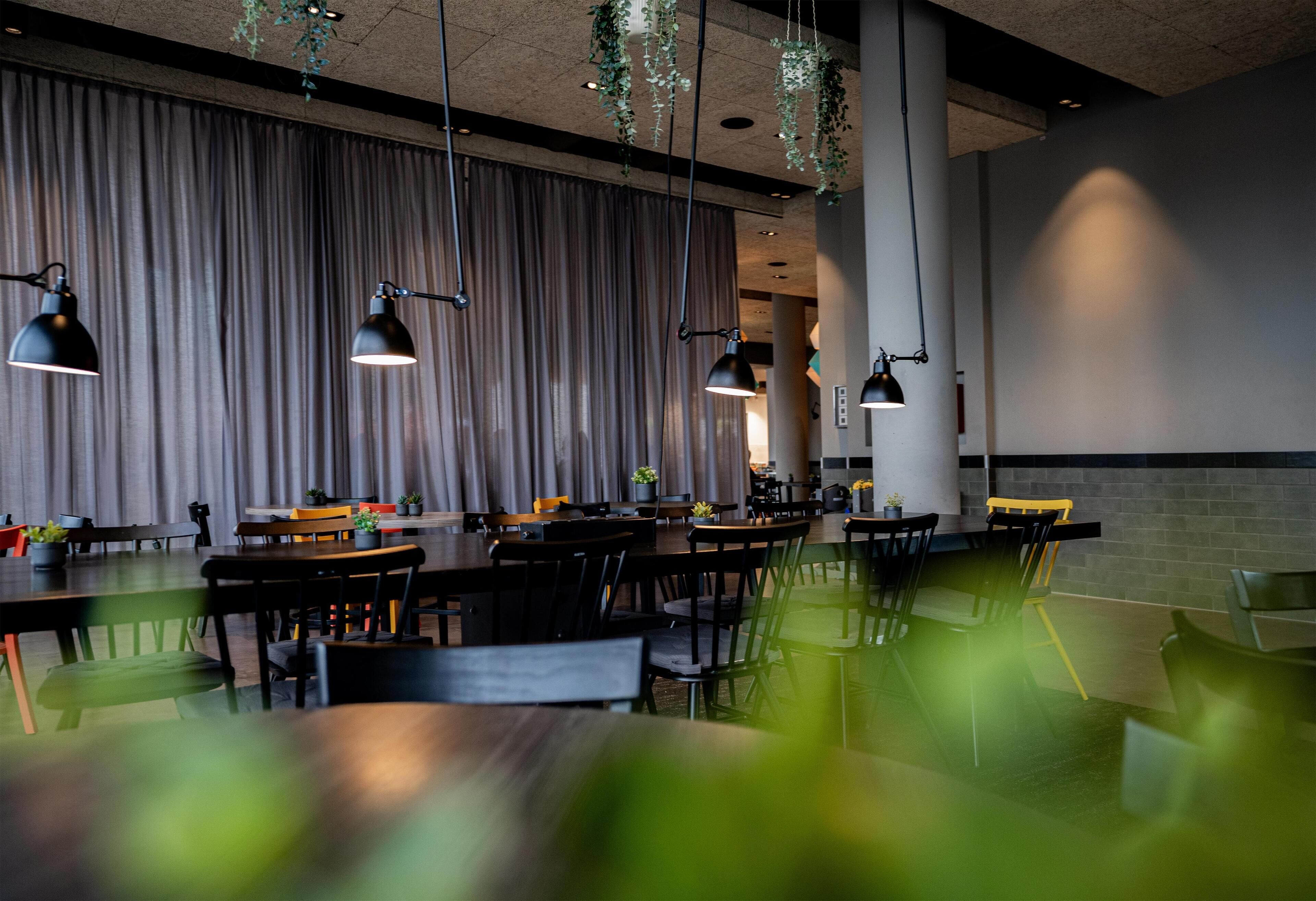 A modern dining area with multiple tables and chairs, pendant lighting, and a large curtain backdrop.