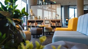A modern lounge area with seating, a bookshelf, and a view of the city. - harry's home Salzburg (Salzburg)