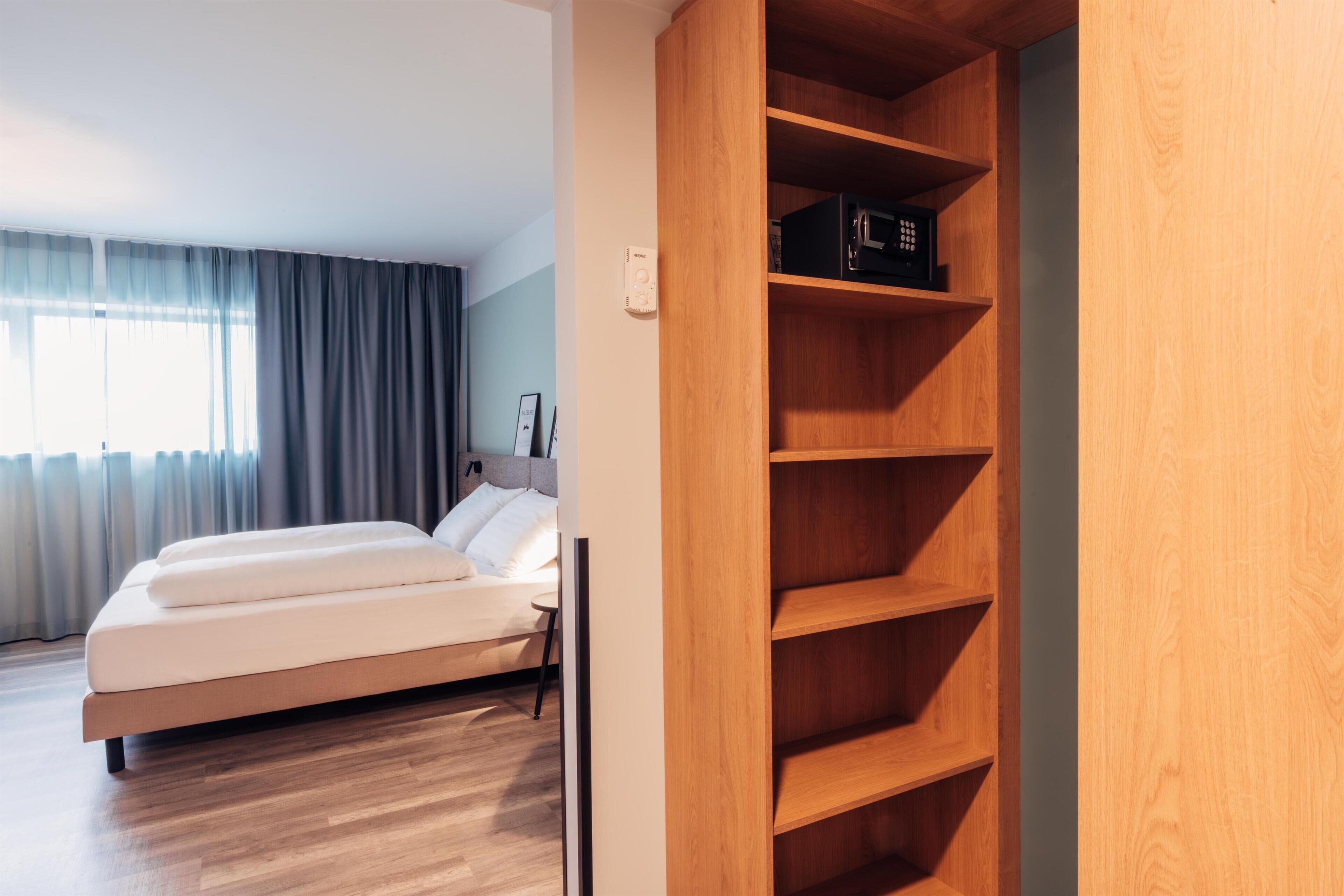 A modern hotel room with a wooden bed, a built-in wardrobe, and a bedside table.