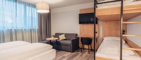 Une chambre d’hôtel moderne équipée d’un lit superposé, d’un canapé, d’un bureau et d’une télévision.