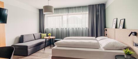 Quarto de hotel moderno com uma cama grande, um sofá, uma mesinha e uma televisão.