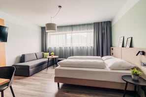 A modern hotel room with a large bed, a sofa, a small table, and a TV.