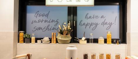 A breakfast bar with a variety of food items and a decorative sign above the window.
