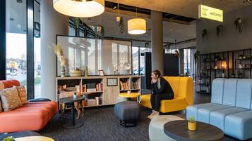 A modern hotel lobby with seating areas, a reception desk, and a large window offering a view of the city.