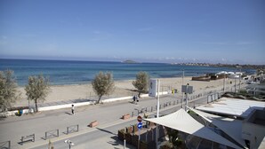 Une route côtière bordée d’une plage, d’un trottoir et offrant une vue dégagée sur la mer.