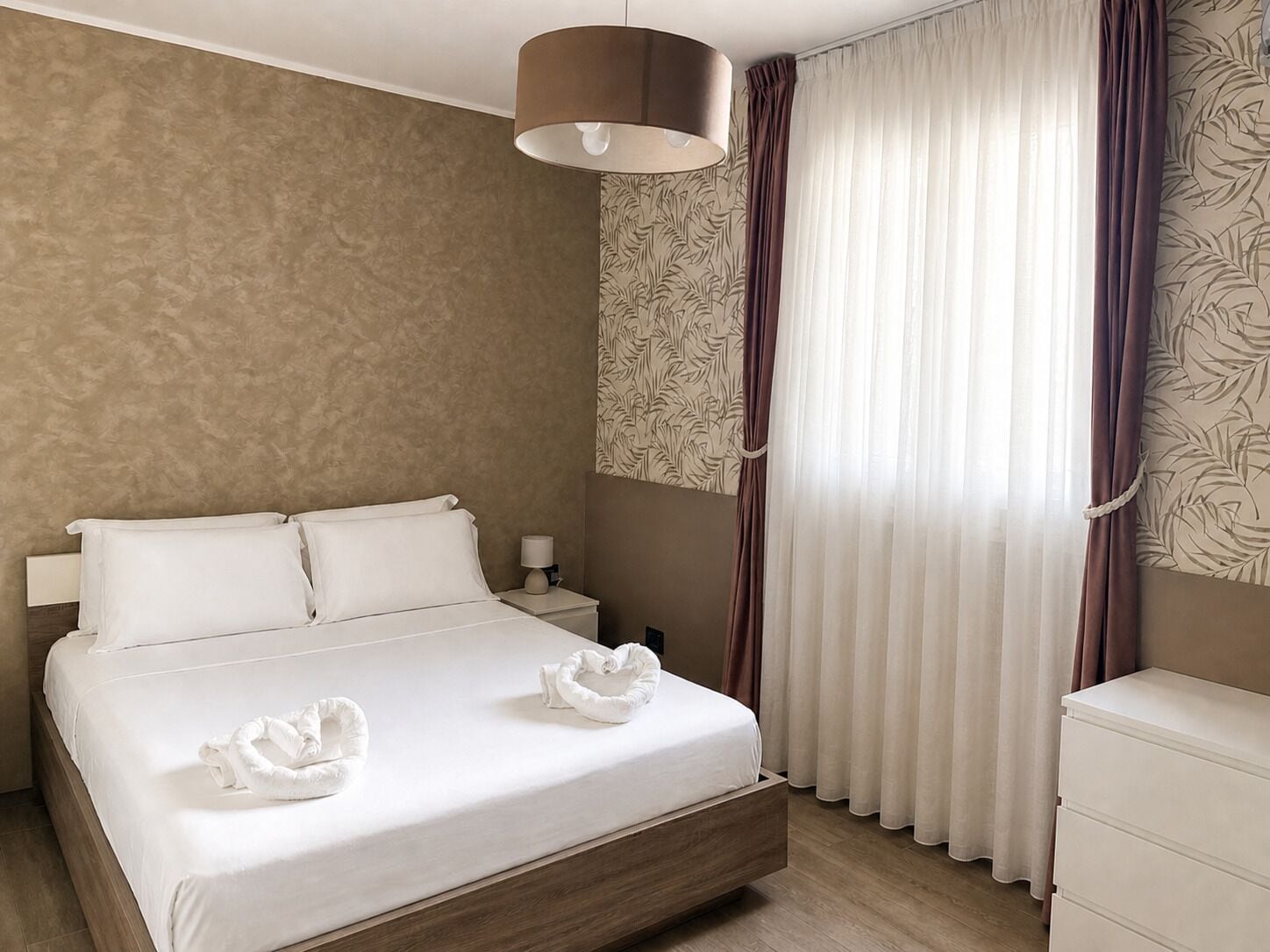 Ein Hotelzimmer mit einem Bett, einem Nachttisch, einer Lampe und einem Fenster mit Vorhängen.