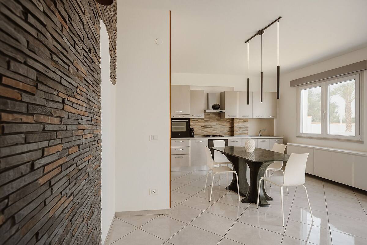 Een moderne keuken met een stenen muur, roestvrijstalen apparatuur en een eethoek met een tafel en stoelen.