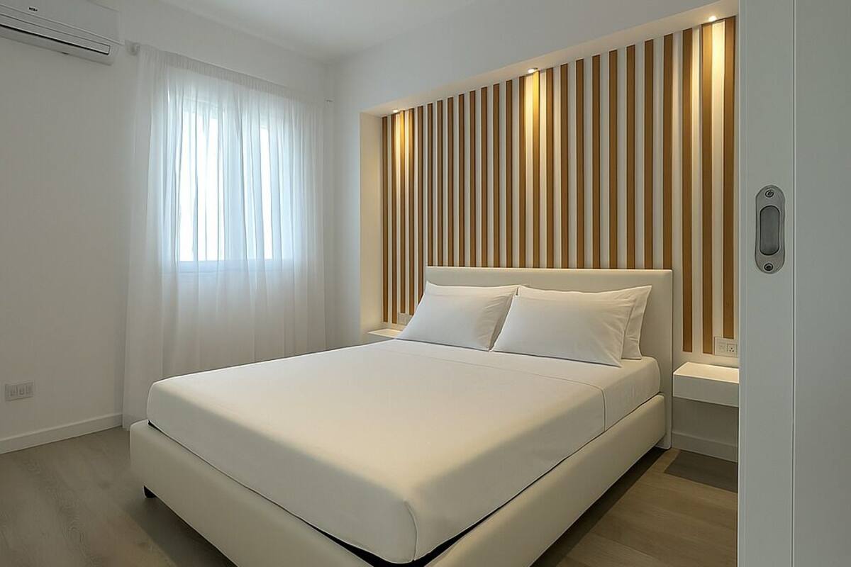 Een moderne slaapkamer met een groot bed, een houten latten hoofd, een nachtkastje en een raam met dunne gordijnen.