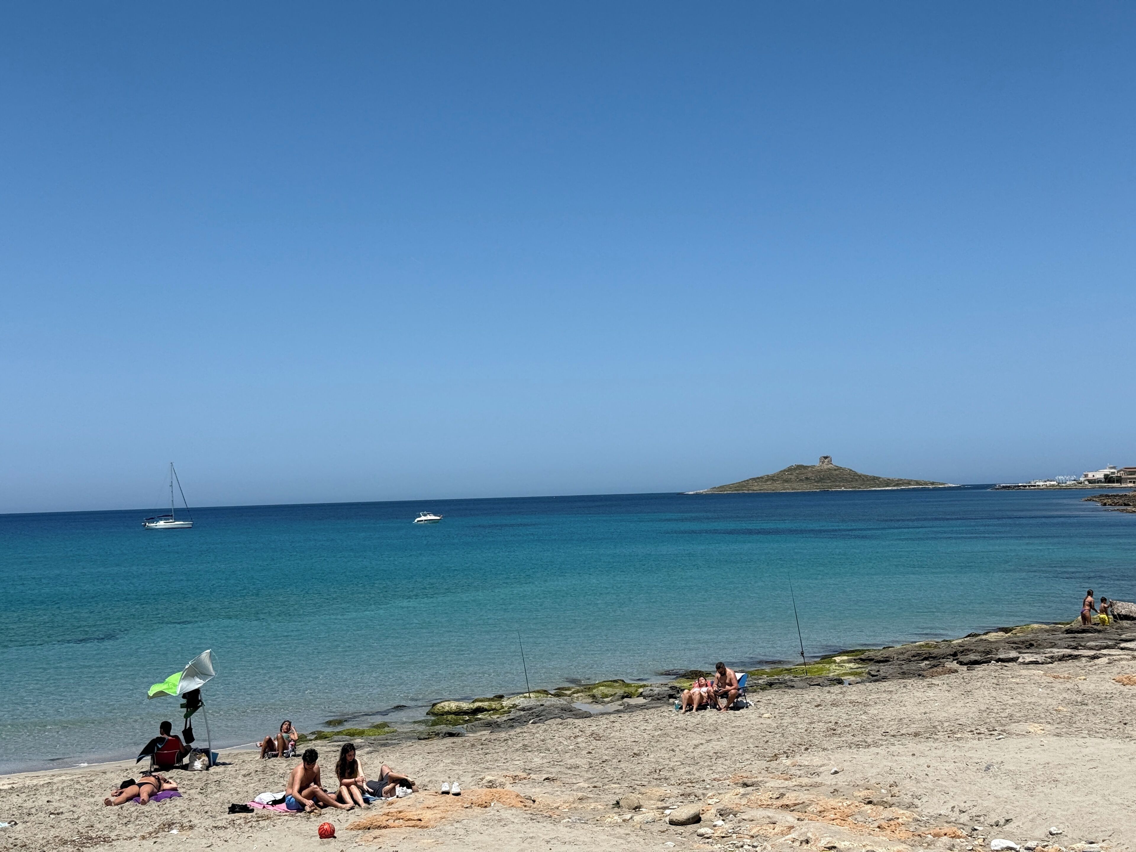 Une plage avec un ciel dégagé, une eau calme et une colline qui se dessine à l’horizon.