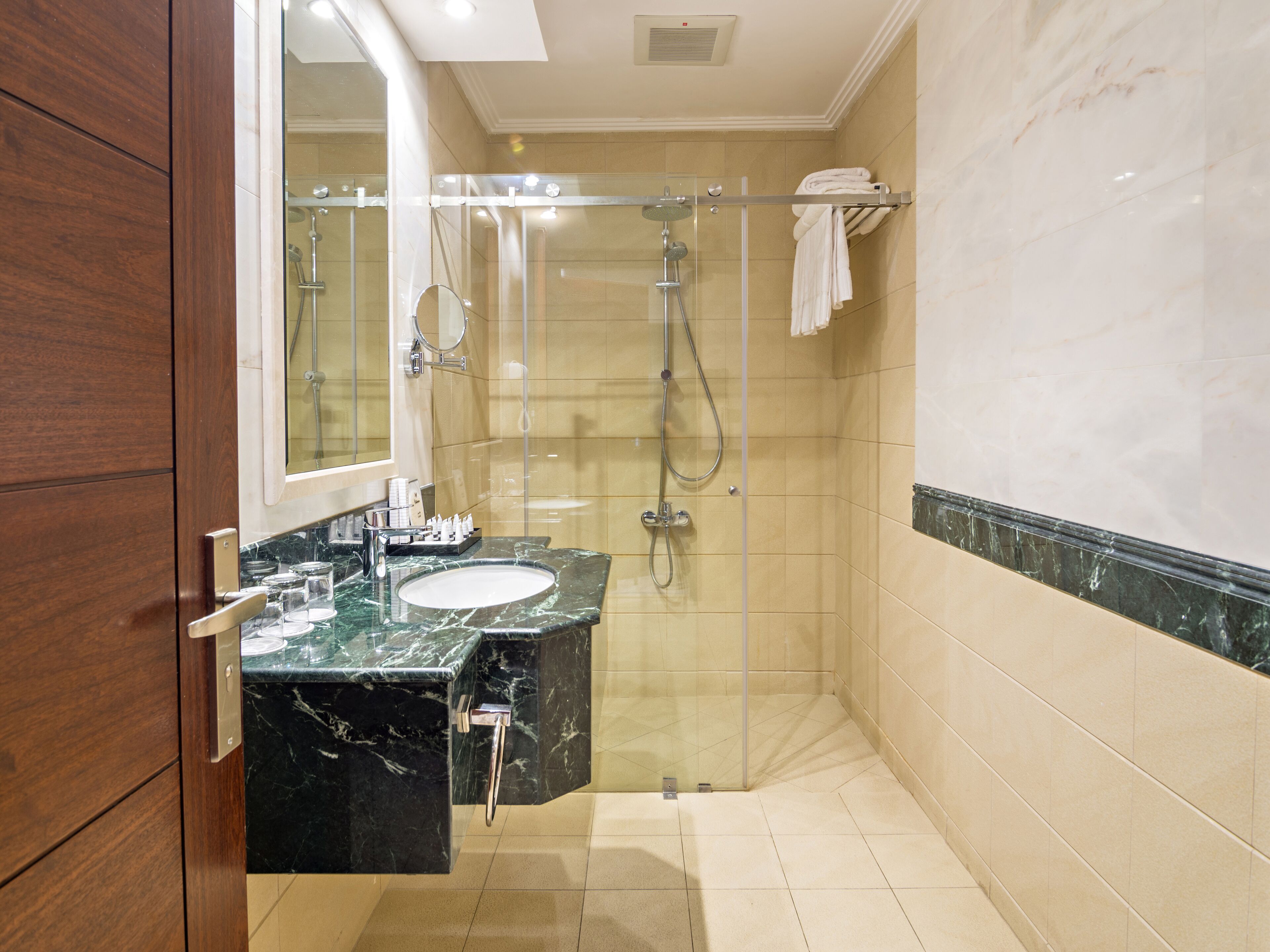 Un baño moderno con ducha de vidrio, lavamanos de mármol y tocador de madera.