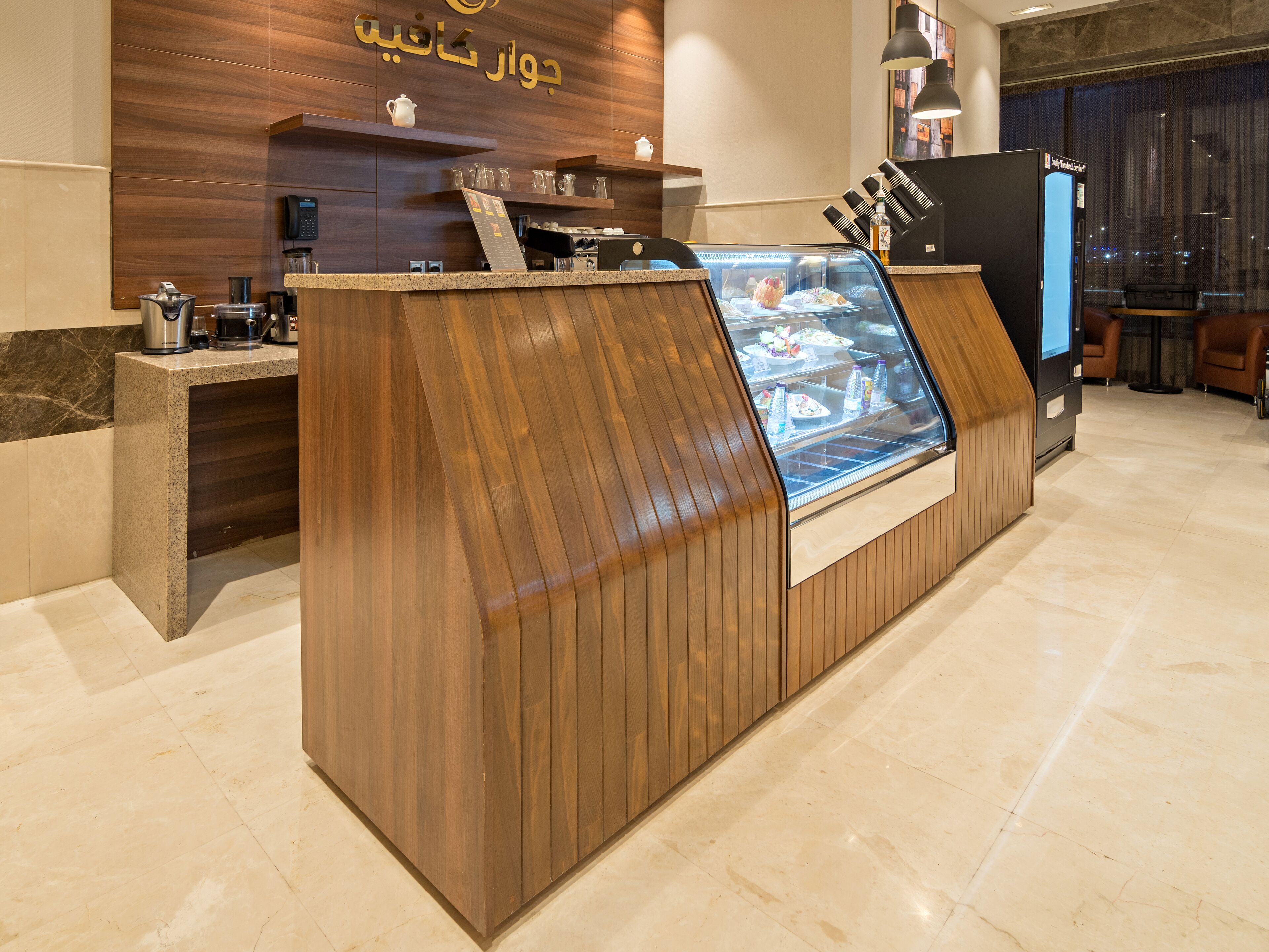 Zona de recepción con mostrador de madera, máquina de café y vitrina con alimentos.