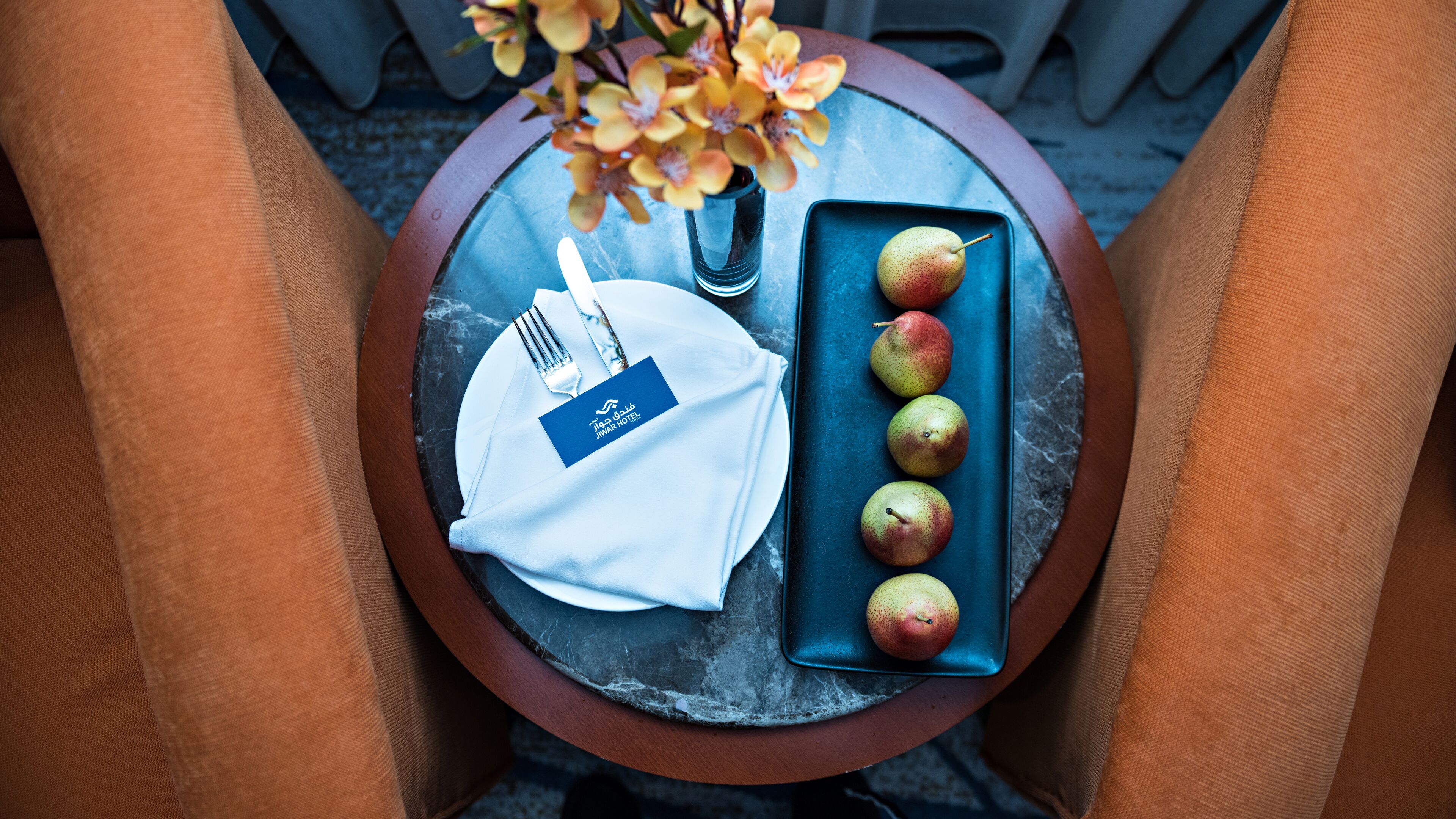 A table with a plate of apples, a napkin, a fork, and a vase with flowers.