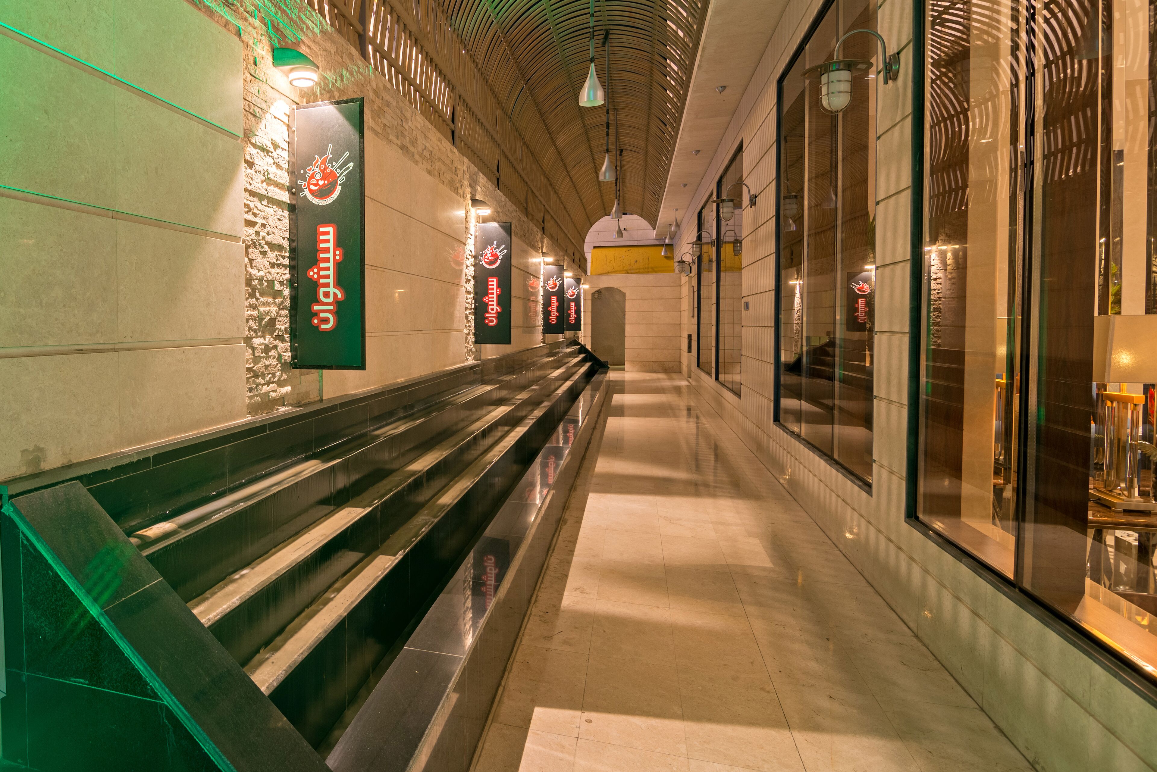 A long, narrow corridor with benches and glass storefronts on one side.