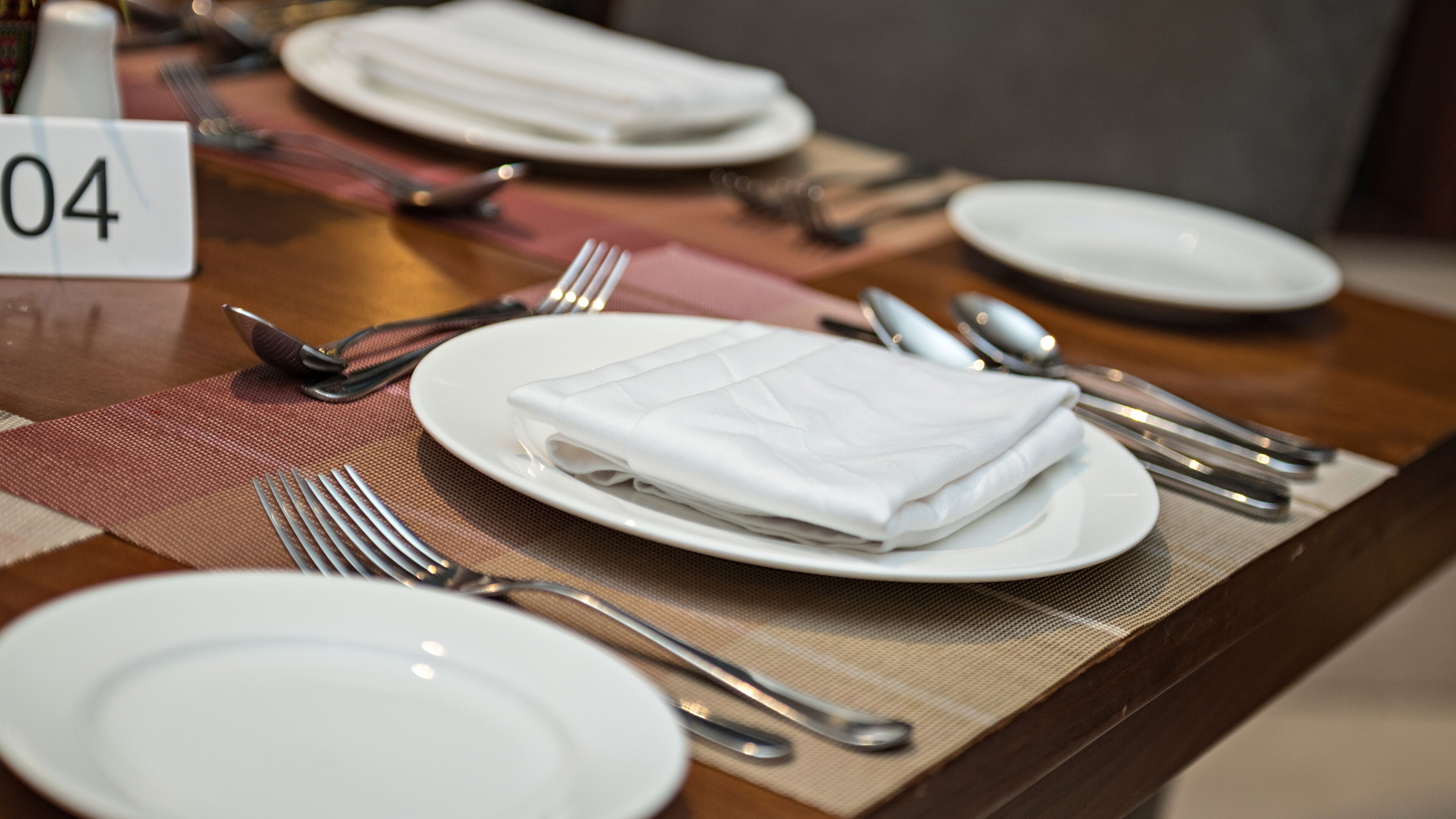 A table set with white plates, silverware, and a folded napkin. A number sign "04" is visible on the table.