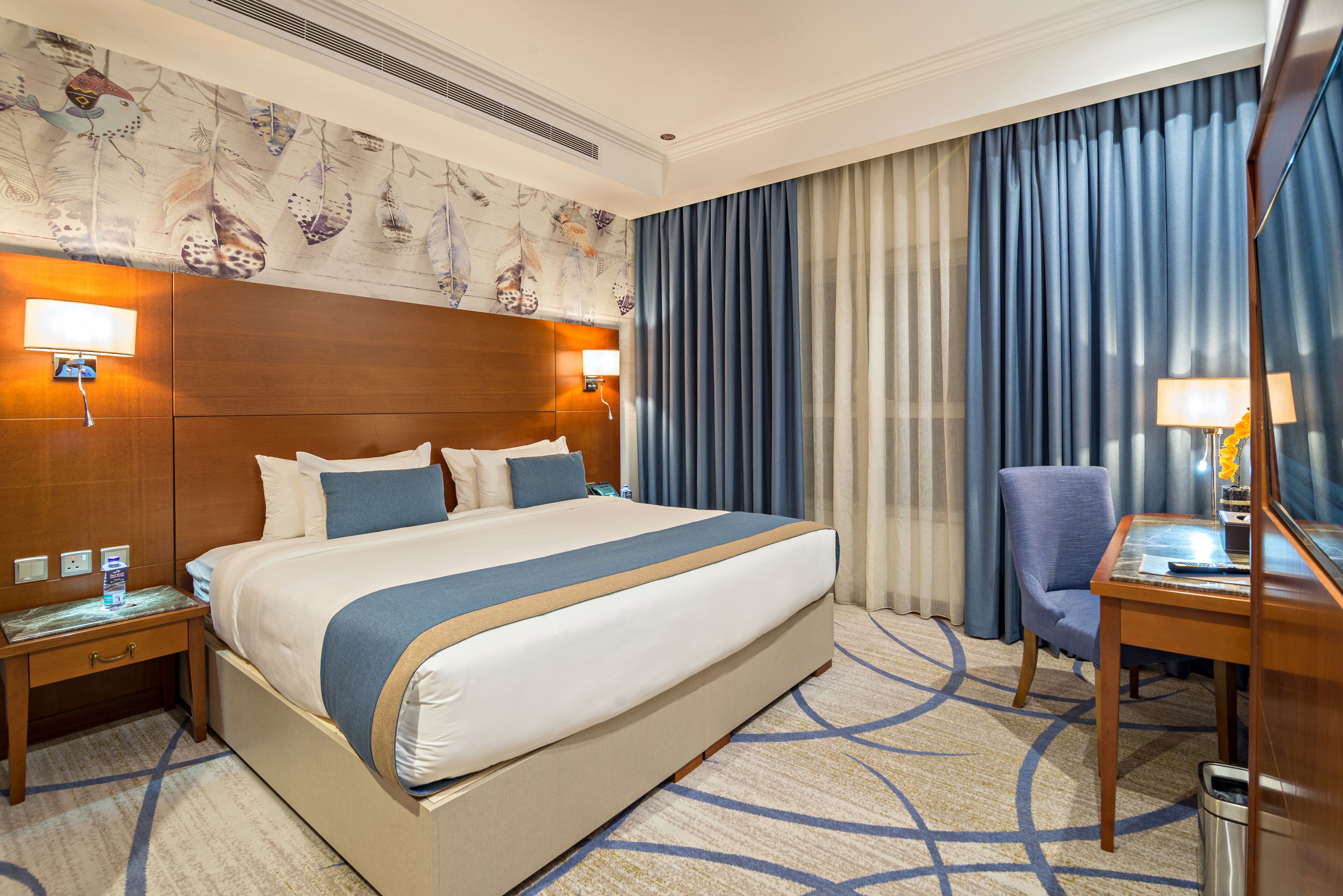 Ein Hotelzimmer mit einem großen Bett, einem Schreibtisch, einem Sessel und einem Nachttisch.