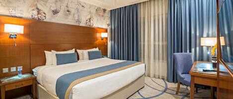 A hotel room with a large bed, a desk, a chair, and a nightstand.