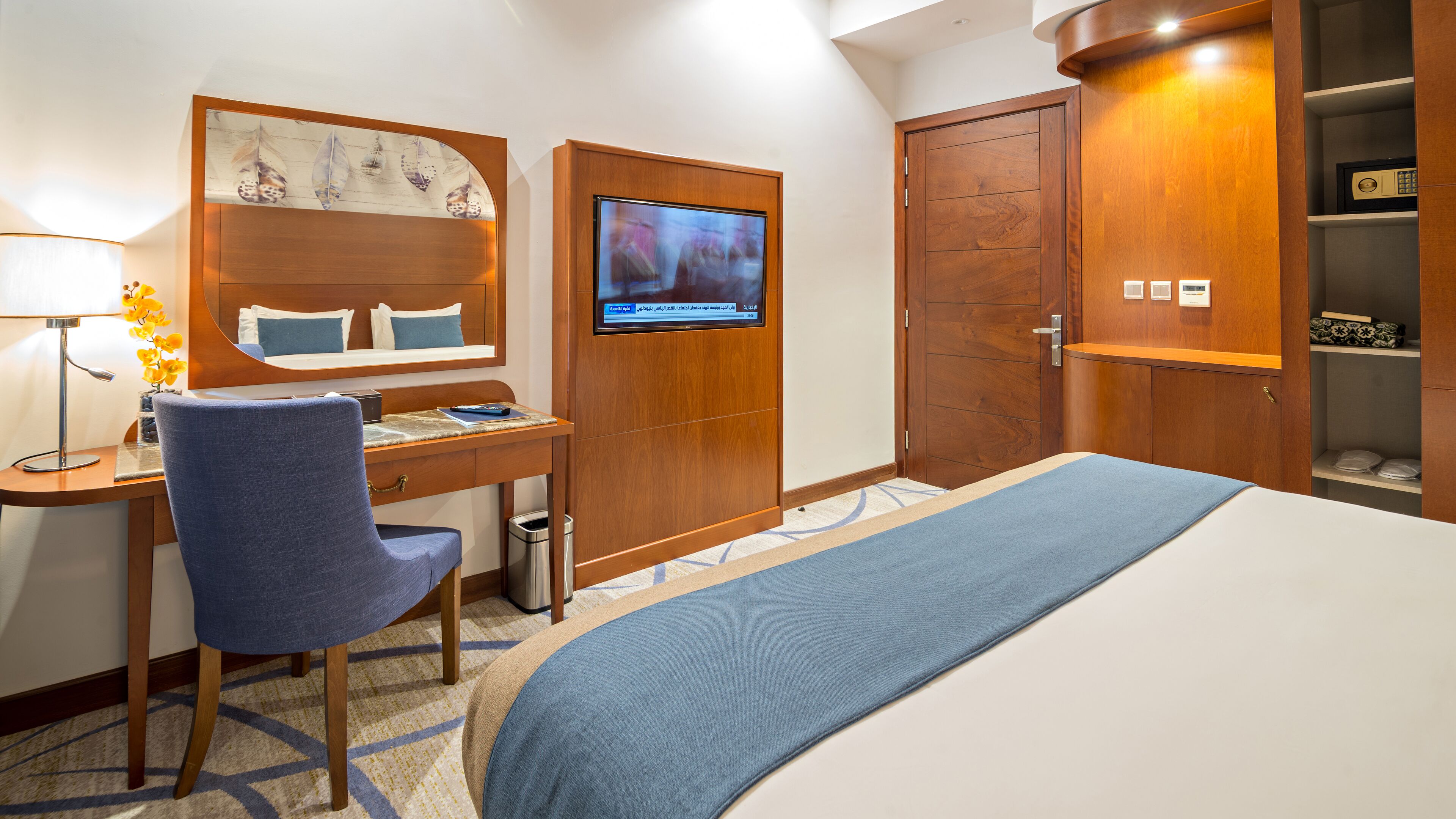 A hotel room with a bed, desk, chair, TV, wardrobe, and a trash bin.