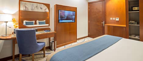 Habitación de hotel con cama, escritorio, silla, televisor, armario y cesto de basura.