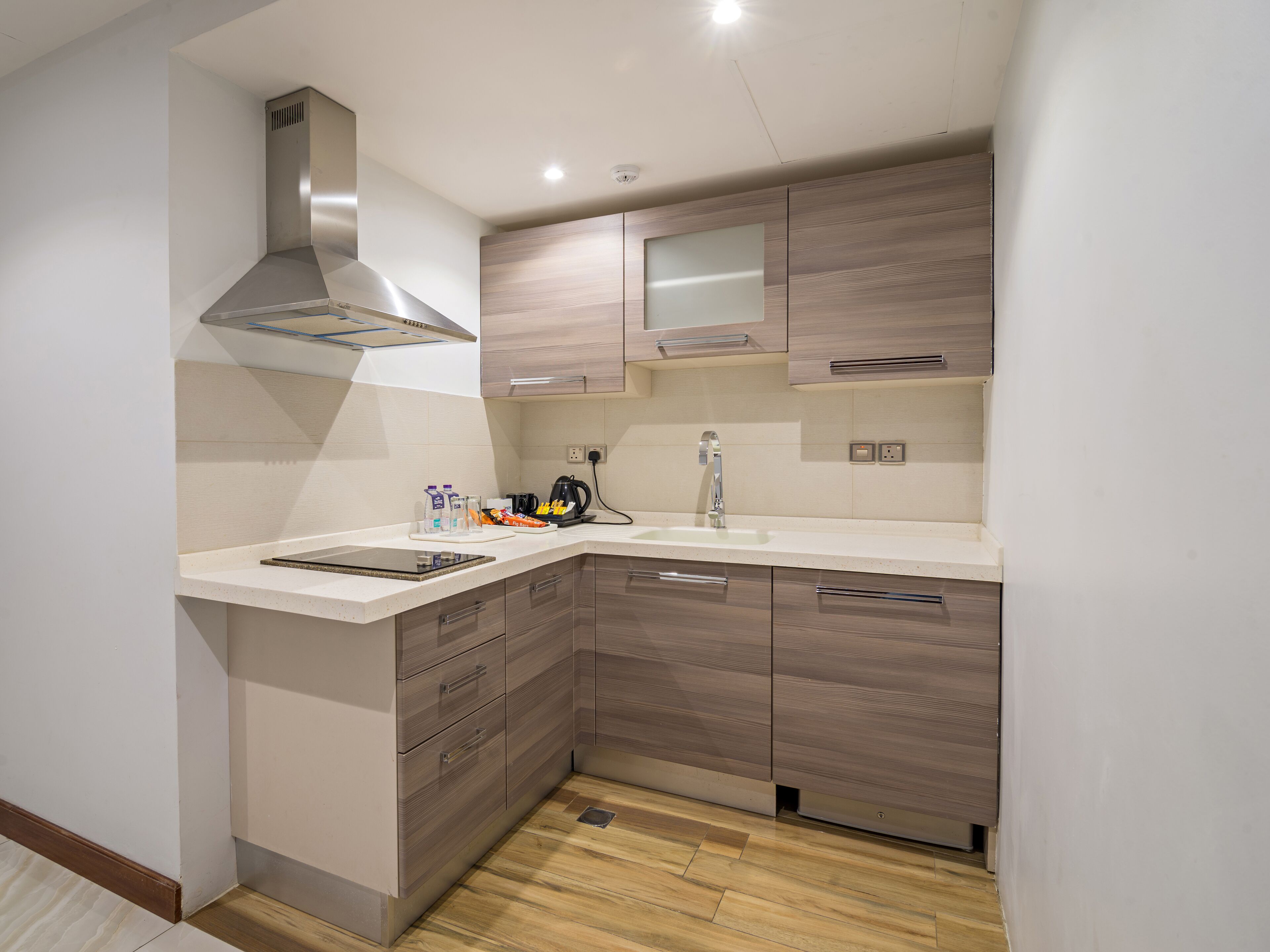 A modern kitchen with wooden cabinets, a stainless steel range hood, and a countertop with various items.