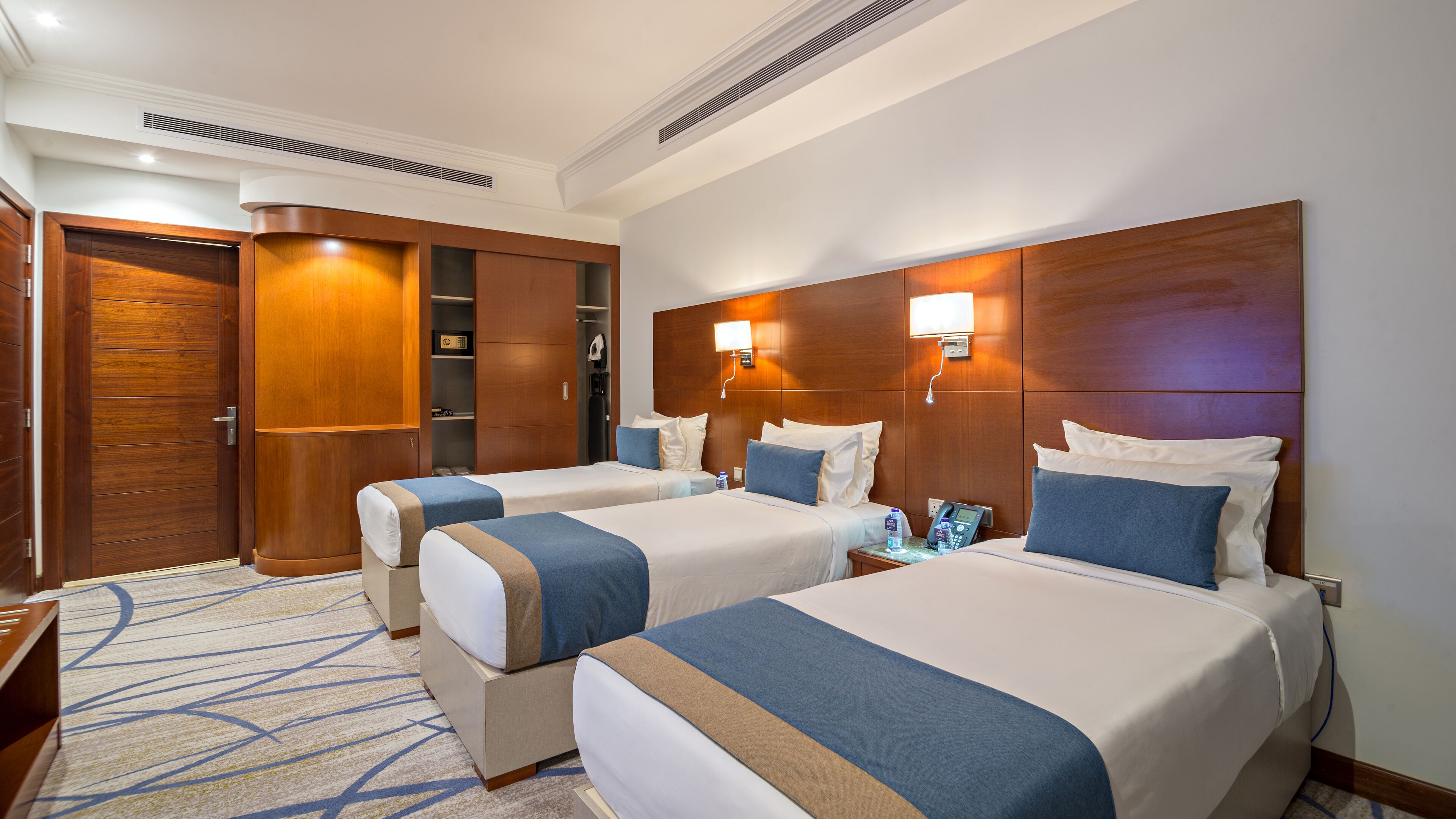 A hotel room with two beds, a wardrobe, a bathroom, and a desk.