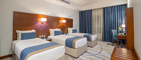 A hotel room with two beds, a desk, and a chair.