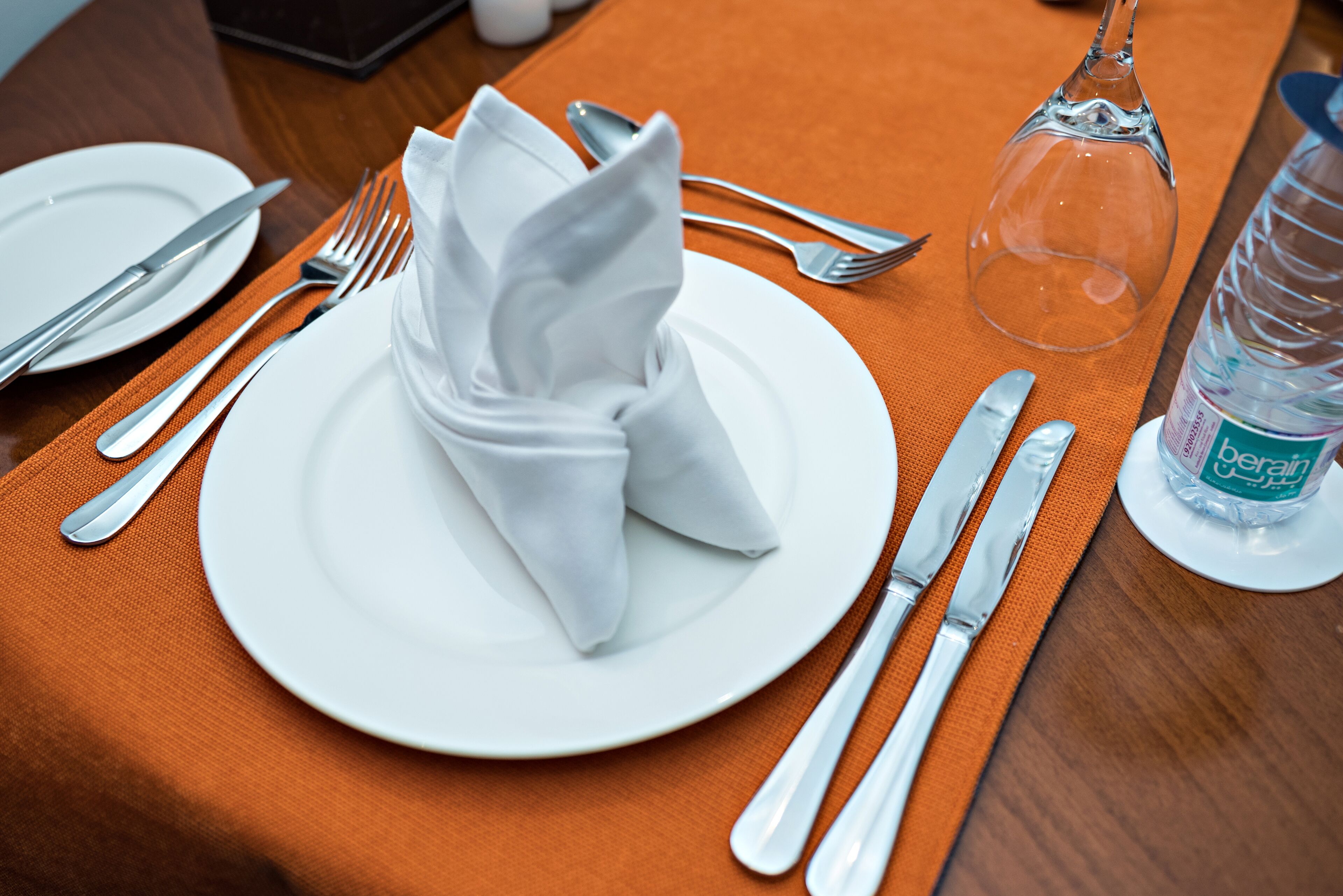 Una mesa de comedor ordenada con un mantel doblado, cubiertos y una botella de agua.