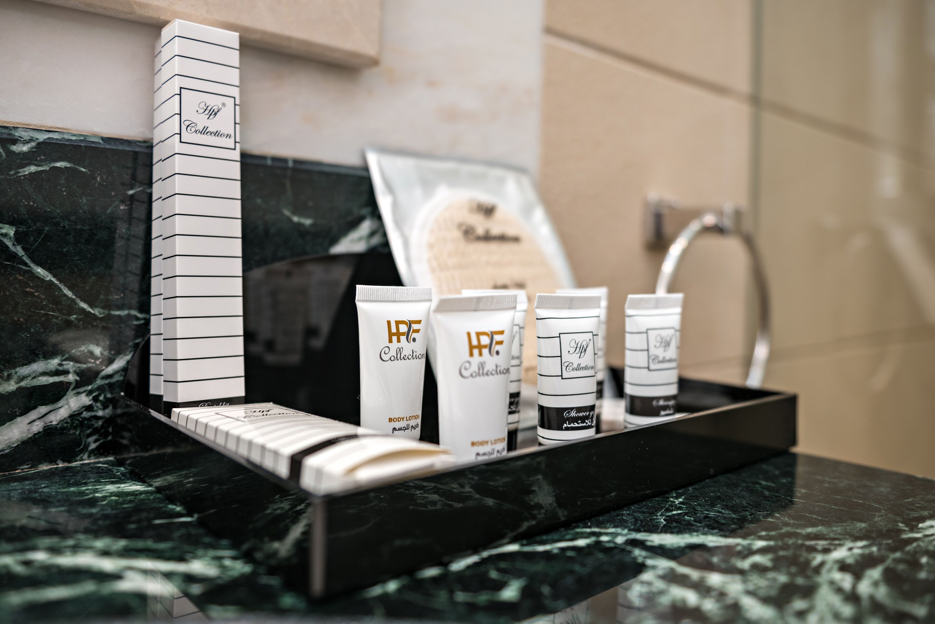 Una encimera de baño con superficie de mármol negro, un libro blanco alto y varios artículos de aseo, incluyendo loción corporal y gel de ducha de la colección 'Hf Collection'.