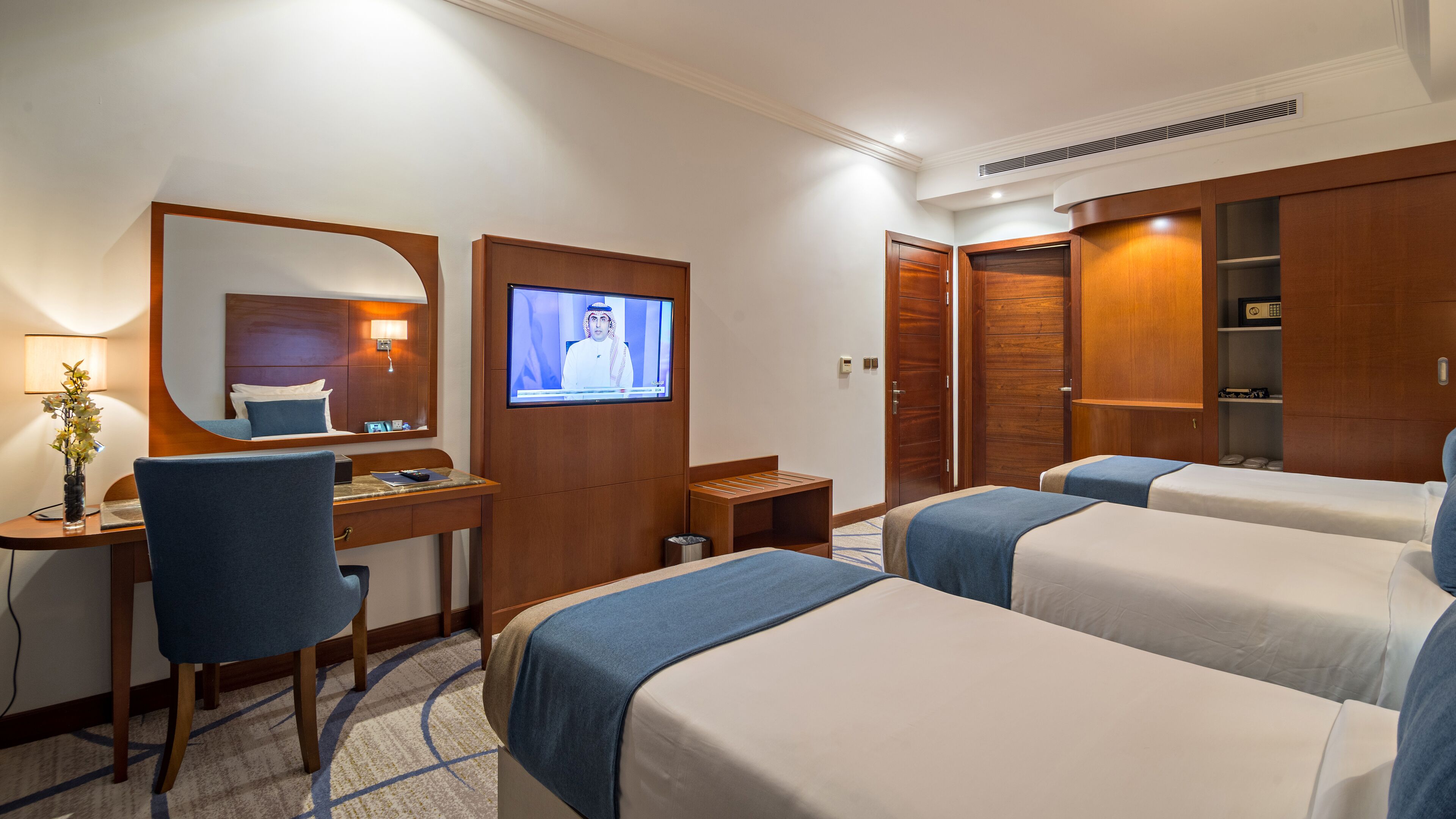 A hotel room with two beds, a desk, a chair, a TV, and a wardrobe.