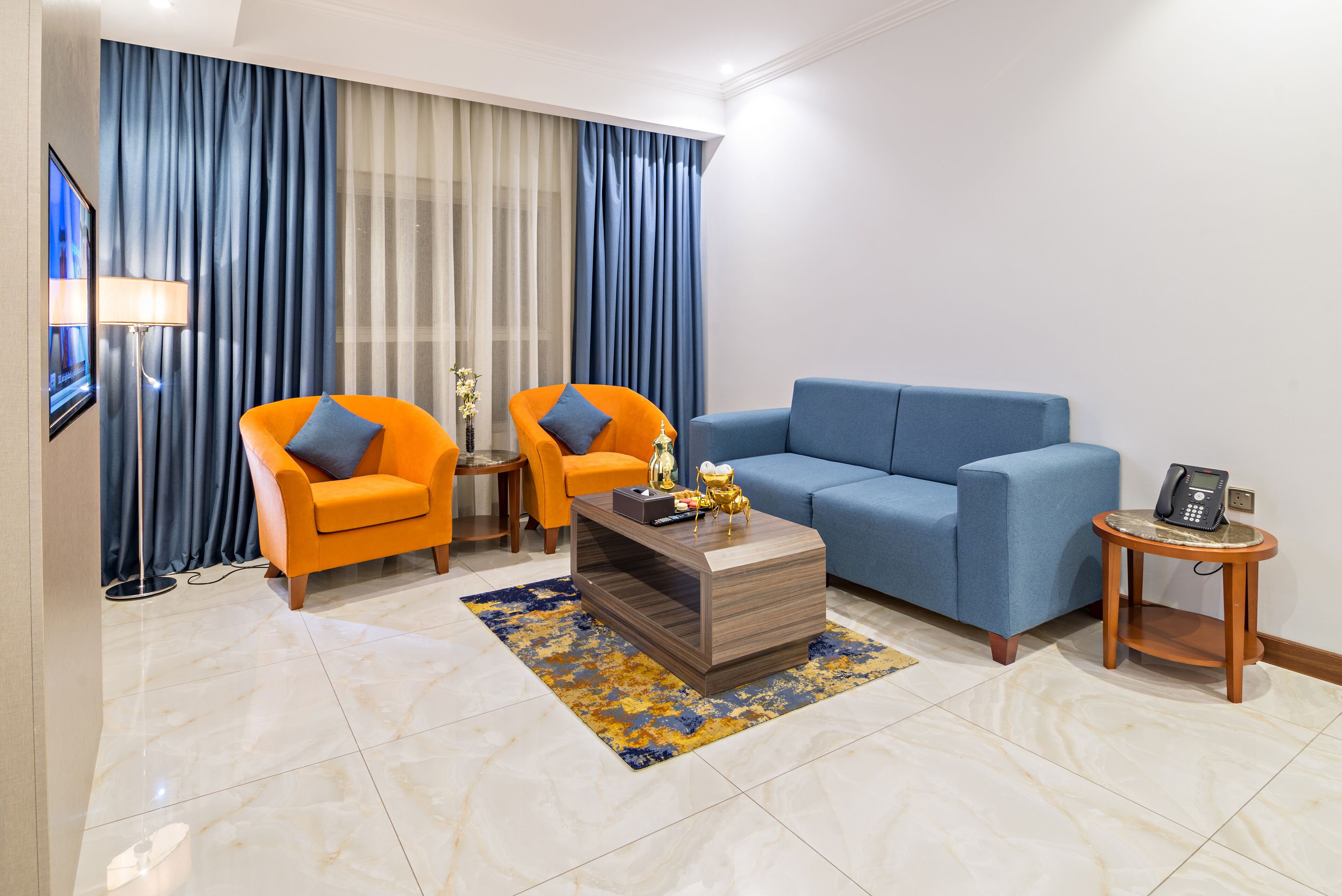 A modern living room with a blue sofa, two orange armchairs, a coffee table, and a small side table with a phone.