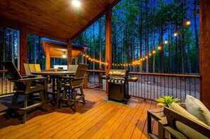 Une terrasse extérieure équipée d’un barbecue, d’un espace salon et offrant une vue sur une forêt.