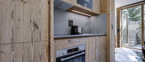 A modern kitchen with wooden cabinetry, a built-in oven, a microwave, and a countertop with a coffee maker.