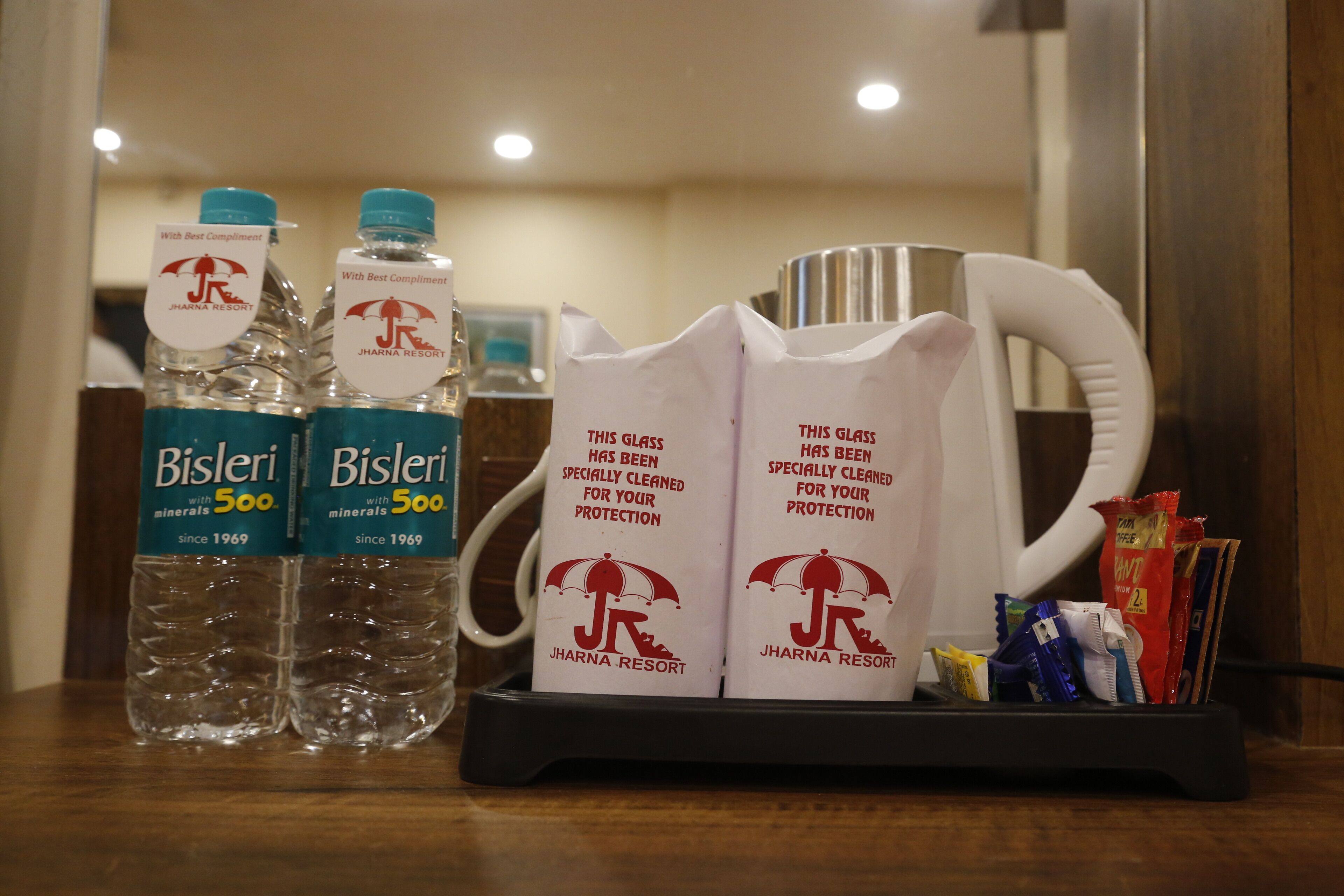 Uma mesa de hotel com duas garrafas de água Bisleri, duas canecas personalizadas e um tabuleiro com diversos petiscos.