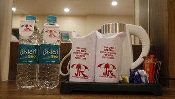 Uma mesa de hotel com duas garrafas de água Bisleri, duas canecas personalizadas e um tabuleiro com diversos petiscos.