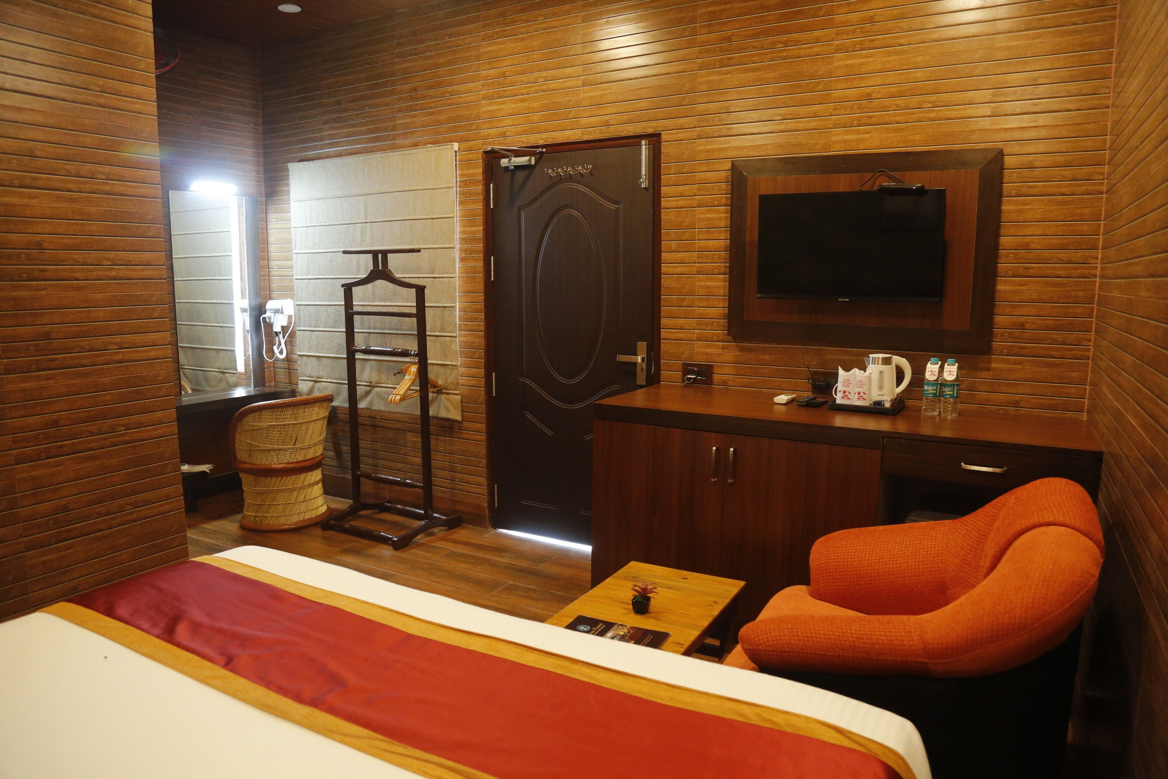 A hotel room with a wooden wall, a bed with a red and white bedspread, a wooden desk with a television, and a chair.