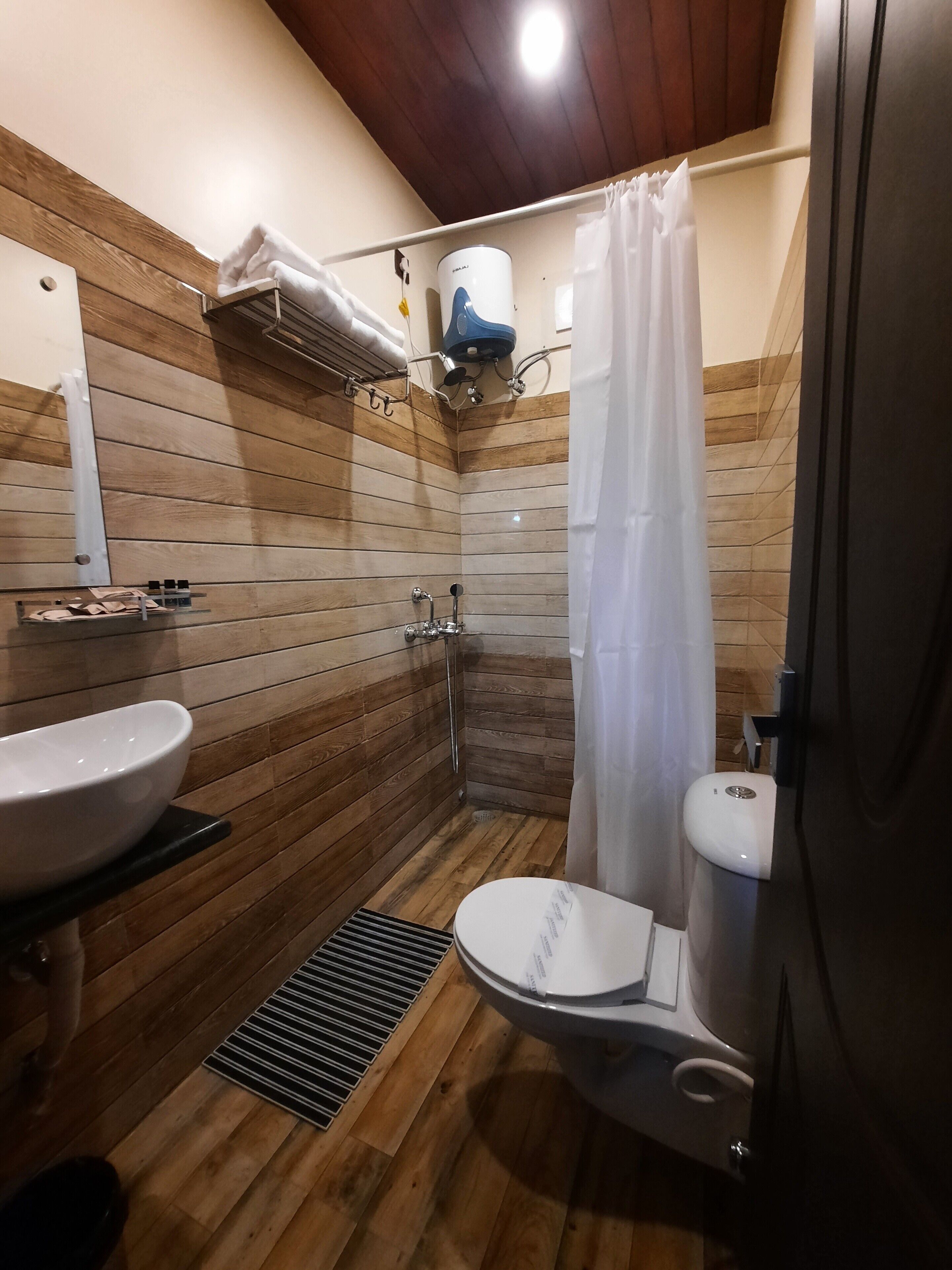 A bathroom with a wooden floor, a white sink, a toilet, and a shower area with a curtain.