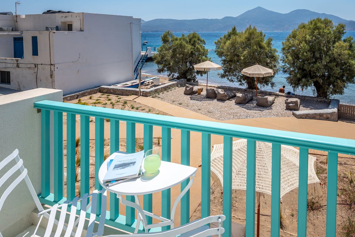 A balcony with a view of a beach, a table with a glass, and a chair.