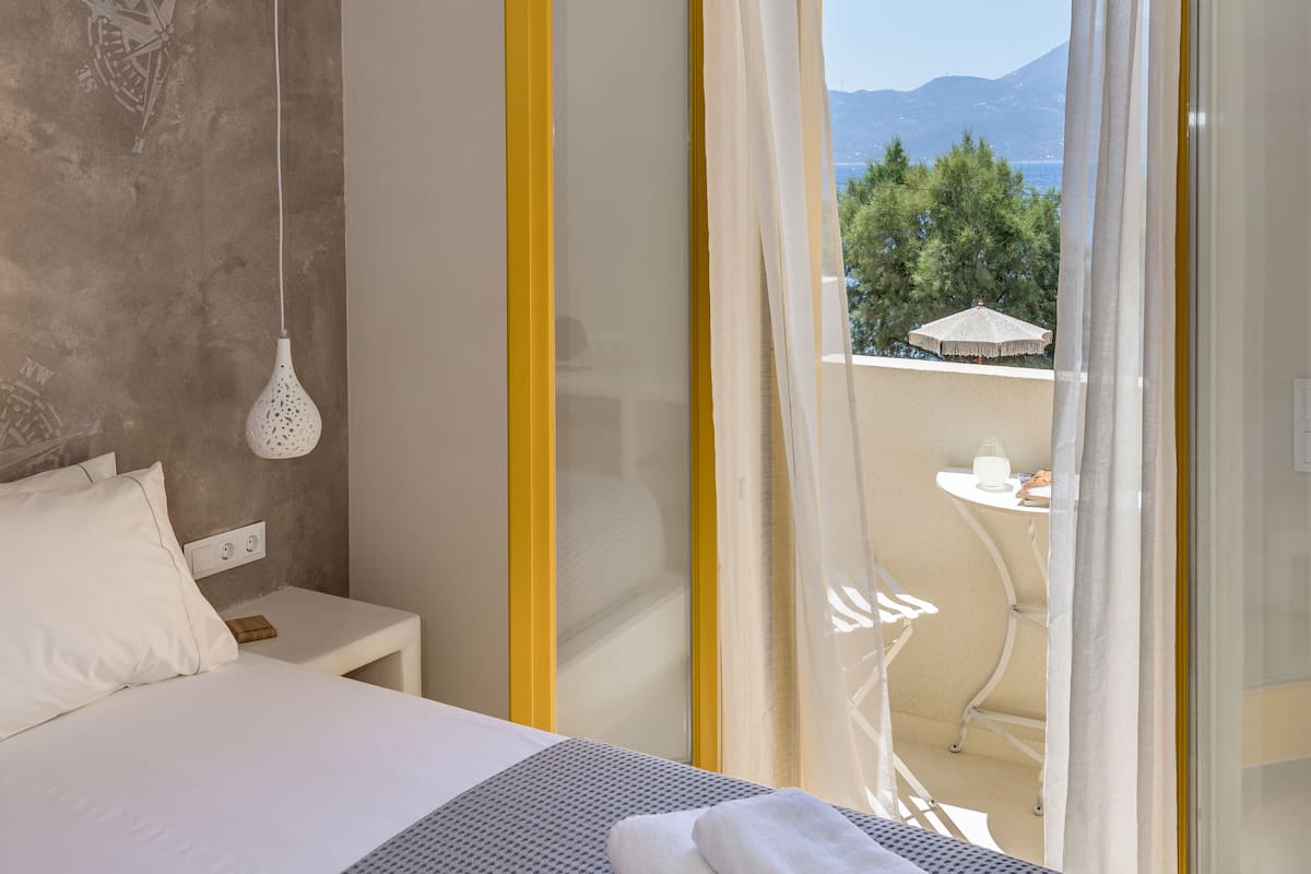 A hotel room with a bed, a bedside table, a hanging light fixture, and a view of the outdoors through a sliding glass door.
