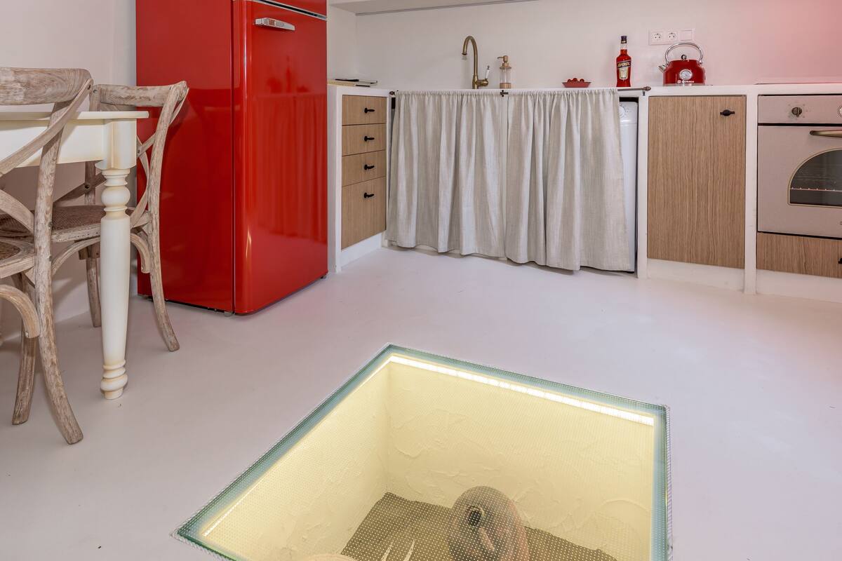A modern kitchen with a red refrigerator, wooden cabinets, a white countertop, and a small sink.