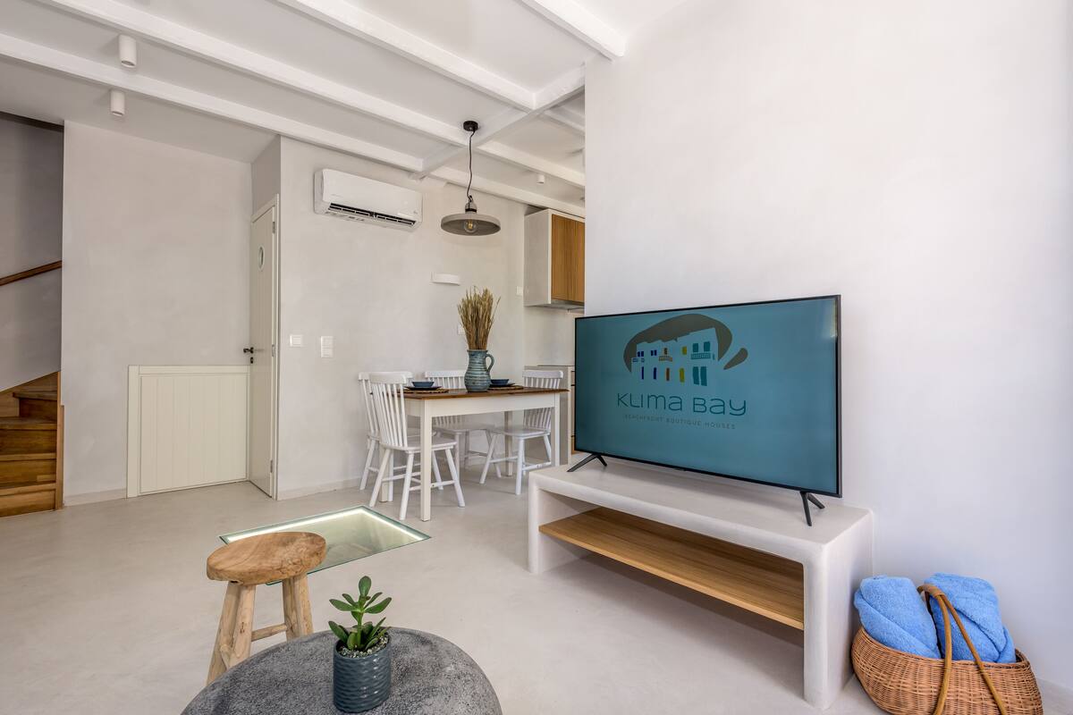 A modern living room with a flat-screen TV, a dining area, and a staircase.