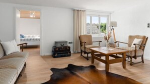 A living room with a sofa, two armchairs, a wooden coffee table, and a leather rug. There are suitcases stacked against the wall and a window with curtains. - Cozy vacation home Zur Alten Burg/Family reunion/Edersee (Vöhl)