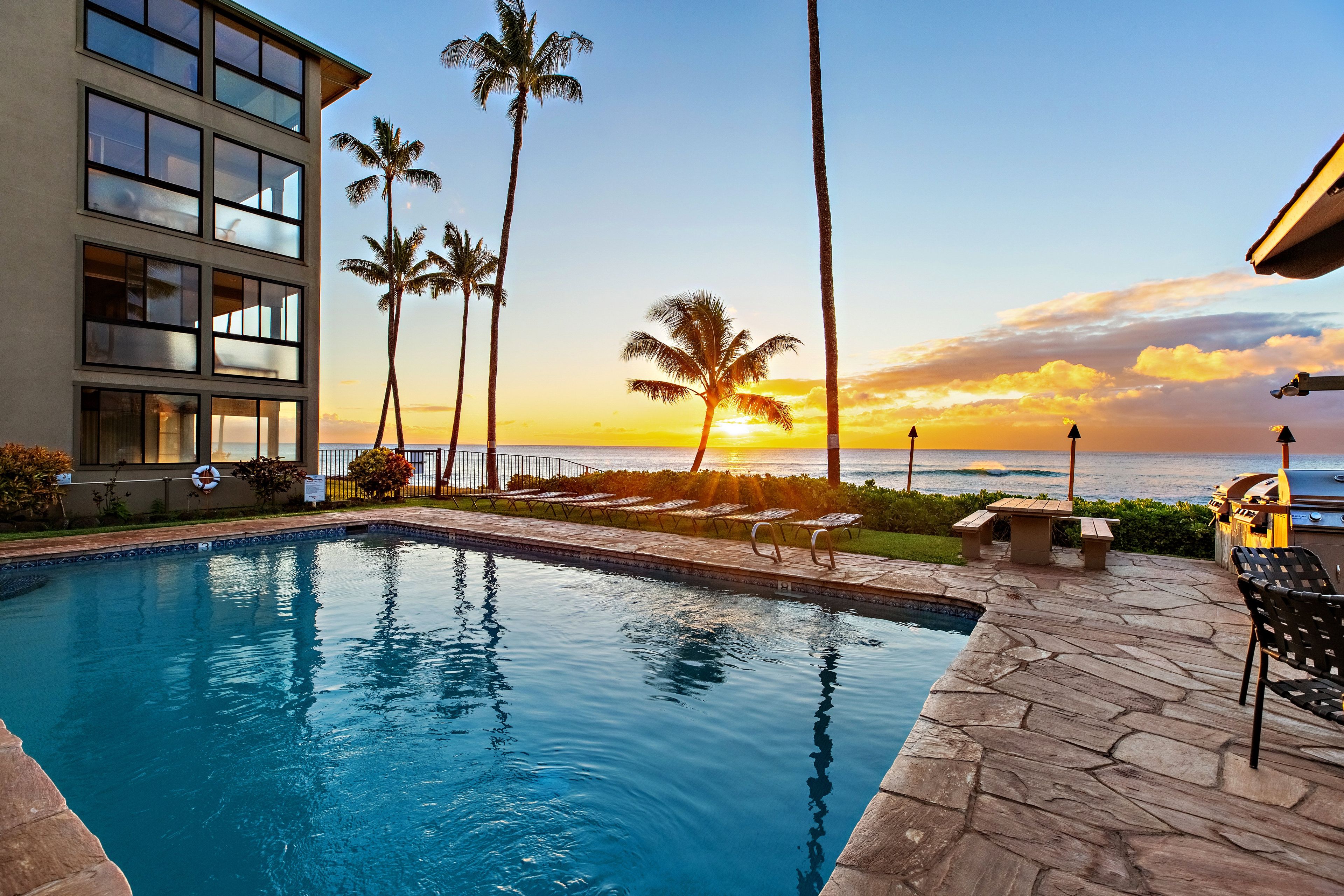 A swimming pool with a sunset view, palm trees, and a building with large windows.