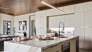 A modern kitchen with a marble island, stainless steel appliances, and a wooden ceiling.