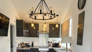 A modern kitchen with dark cabinets, a central island, and pendant lighting. There is a gray sofa with cushions and a small rug in the living area. - Stunning One Bed Modern & Contemporary Chalet (Bridlington)