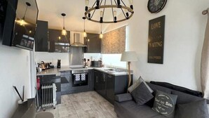A modern kitchen with a central island, a dining area with a sofa, and a living room with a fireplace. - Stunning One Bed Modern & Contemporary Chalet (Bridlington)